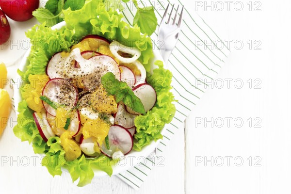 Radish, onion and orange salad with mint, vegetable oil and spices on lettuce in a plate on a towel