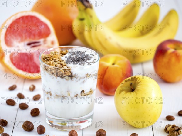 Healthy breakfast: yogurt with muesli and chia seeds, fruits and nuts on white wooden background.