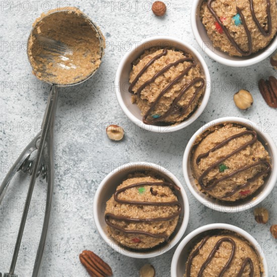 Safe-to-eat raw monster cookie dough in small portion bowl, ice cream scoop and nuts on gray cement