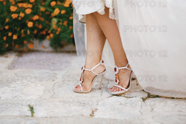 Bride's legs in stylish sandals with crystals with high heels peek out from under the wedding