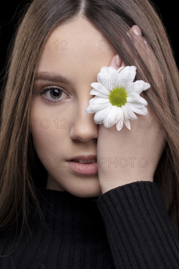 A beautiful girl with natural beauty holds a white flower near her eye. Young girl with a white