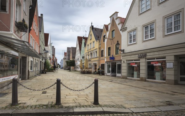 An empty shopping street with historic buildings and shop fronts under a cloudy sky, pedestrian