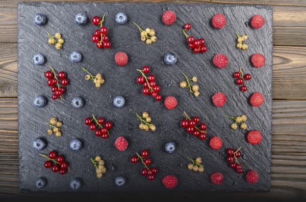 Flat lay view at ripe bilberry raspberry white and red currant on slate stone tray closeup