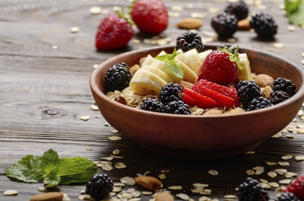 Fruit healthy muesli with banana strawberry almonds and blackberry in clay dish on wooden kitchen