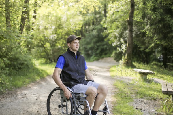Happy and young disabled or handicapped man sitting on a wheelchair in nature turning wheels on a