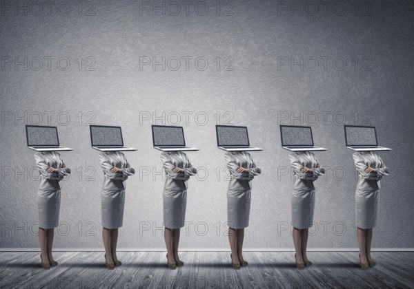 Business women in suits with laptop instead of their heads keeping arms crossed while standing in a
