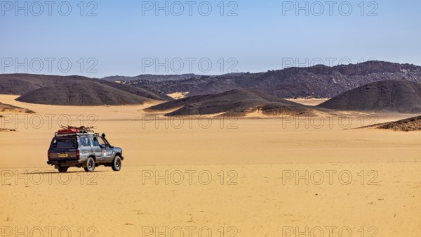 An off-road vehicle stands in vast sand dunes under a clear, sunny sky, off-road through the