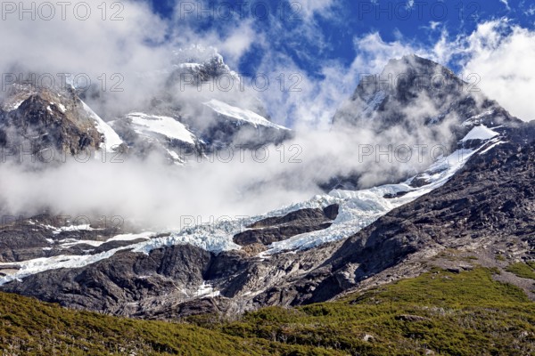 Impressive snow-covered peaks under a clear sky, framed by dramatic clouds, the glaciers of the