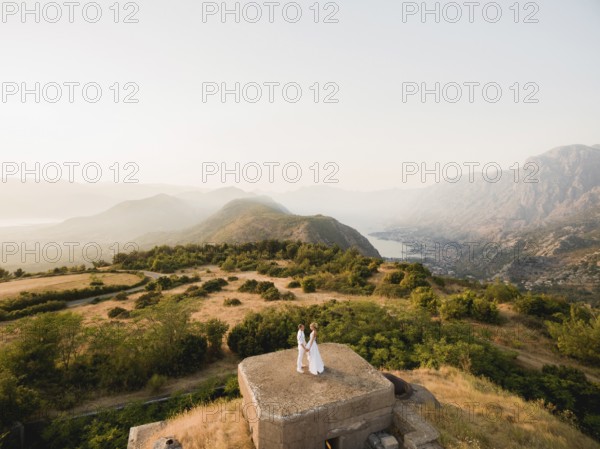 The bride and groom hold hands on the roof of the Gorazda fort, behind them a view of the Bay of