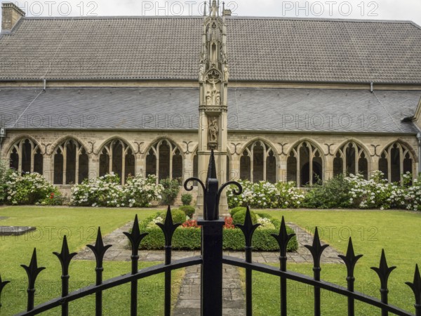 A well-kept courtyard with Gothic architecture, flower beds and a decorative fence in the