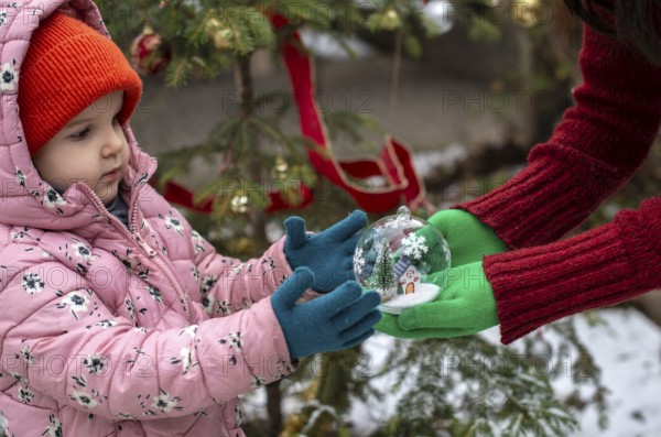 Crystal christmas ball with house and snow inside. Hands with green gloves gives transparent ball