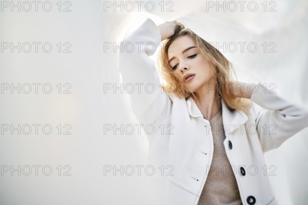 Young attractive woman in white clothes posing on abstract pale background looking at camera
