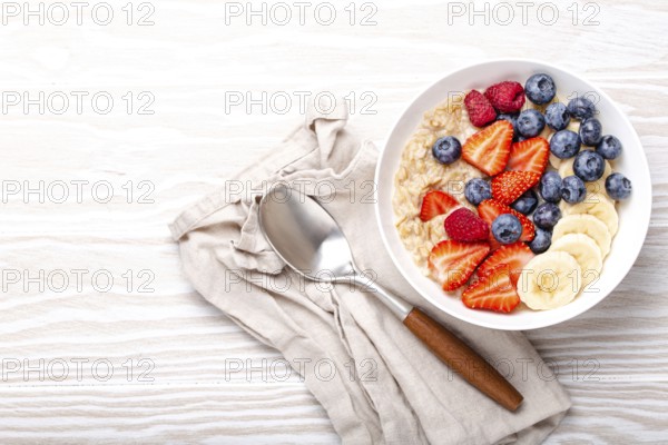 Oatmeal porridge with fruit and berries in bowl with spoon on white wooden background table top