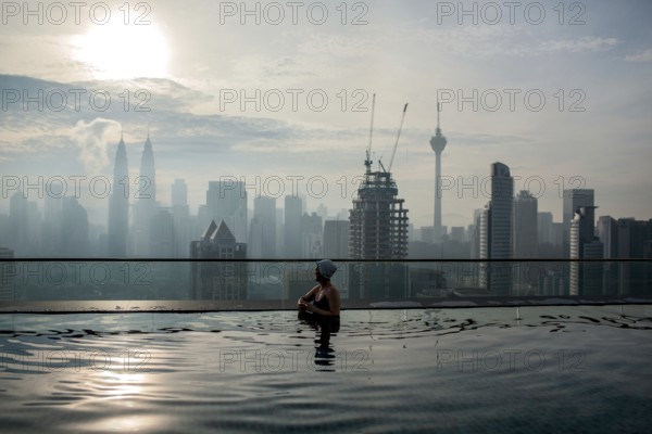 Woman enjoying cityscape of Kuala Lumpur from rooftop swimming pool. Urban scene with skyscrapers,