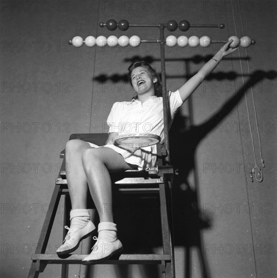 Tennis in the 1940s. A young woman is sitting in the tennis jugdge's chair. The wooden balls in