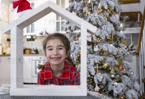 Happy child with tiny house in cozy home with Christmas decor of festive white kitchen. Gift for