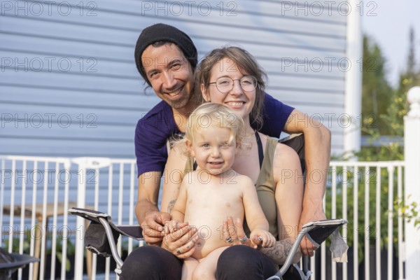 Happy young family pose for group portrait seen from the front. Mother sitting on chair with two