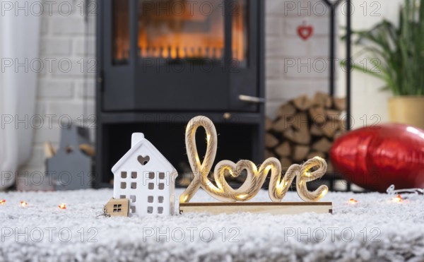 Key to house with keychain against background of fireplace stove with fire and firewood in