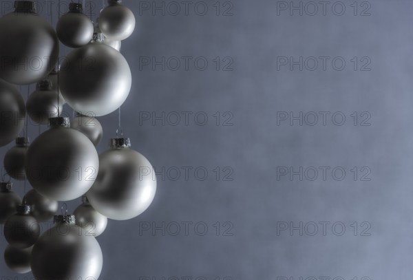 Silver Christmas balls hanged with silver thread, of a matte color, on a gray blurry backdrop,