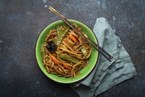 Asian dish stir fry udon noodles with chicken, vegetables and mushrooms in green ceramic bowl with