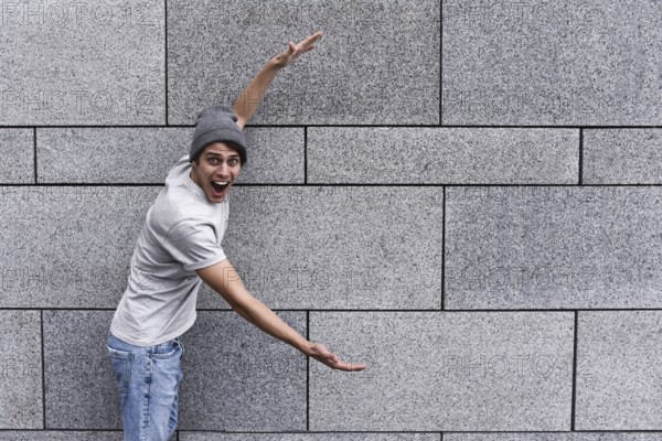 Cheerful guy dressed in gray t-shirt, sunglasses and hat at the street, show a big sale, or nice