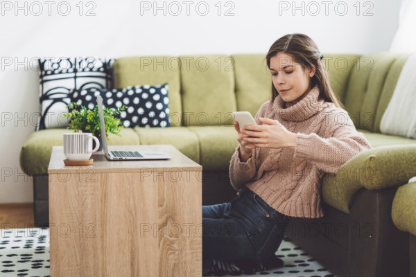 Young caucasian woman with long brown hair in pastel pink sweater and jeans working from home on