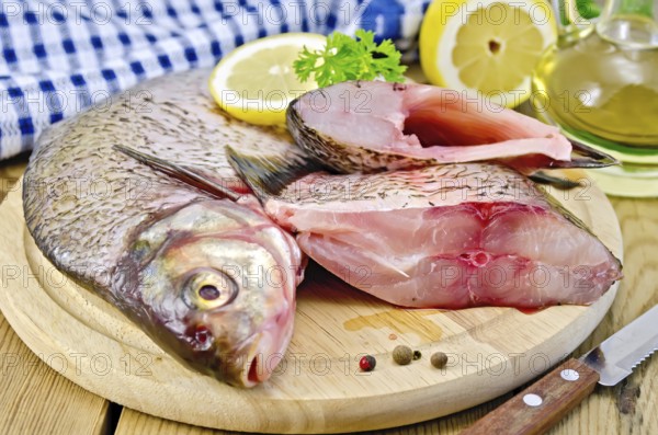 Bream whole peeled and sliced pieces on a round board, parsley, lemon, vegetable oil, napkin, knife