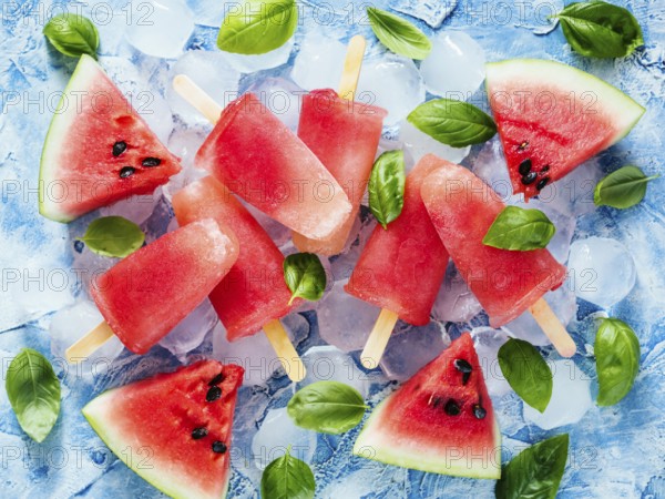 Top view of watermelon and basil popsicles on blue background with fresh green basil leaves and