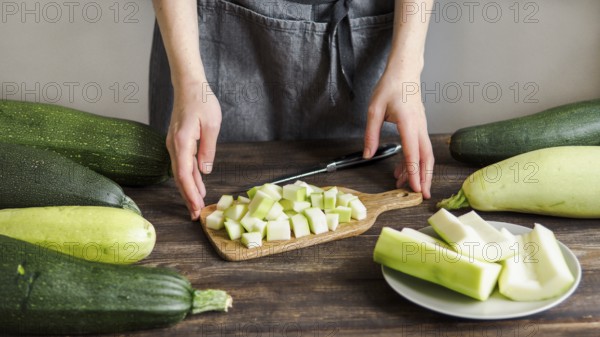 Zucchini harvest. Woman slices zucchini cubes for freezing on wooden table. Farm organic zucchini