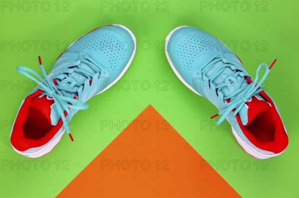 Red, cyan, white pair of new tennis shoes in studio shot over green and orange background. Directly