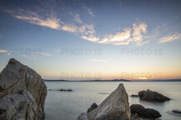 View through rocks on a sandy beach into the sunset. Landscape shot with view to the horizon over