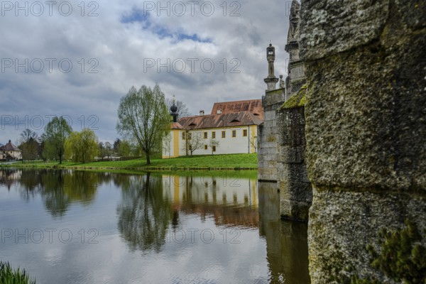 River landscape with stone bridge and historic buildings, reflections on water, cloudy sky,