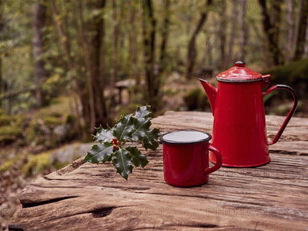 Christmas breakfast in the woods. Sprig of holly next to red mug and vintage coffee pot on wooden