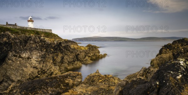 Rocky shoreline with turquoise pools and the historic Broadhaven Lighthouse on a clifftop
