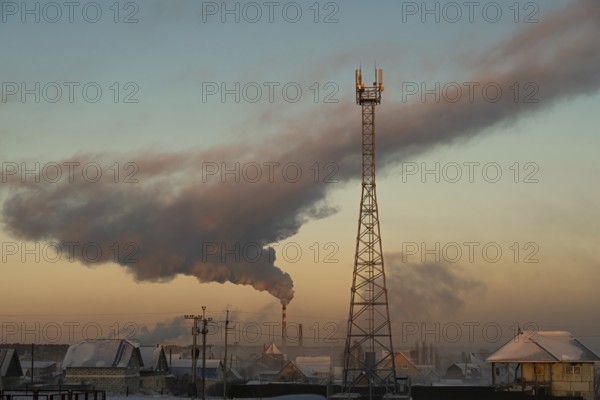 Smoke rises from the chimney of the boiler room over the city and the cell tower is in the