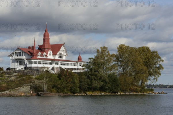 This image captures a historic seaside building with distinctive red roofs, nestled on a small