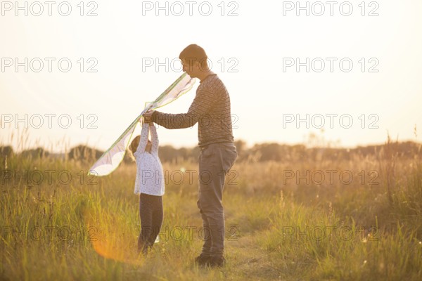 Dad helps his daughter to fly a kite in a field in the summer at sunset. Family entertainment
