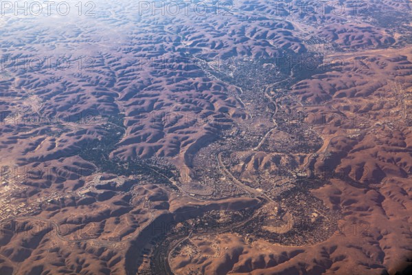 Aerial view of a vast, reddish desert landscape with river valleys and hilly areas, The dunes of