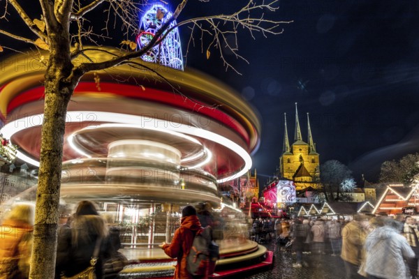 Lebhafte Szene eines Weihnachtsmarktes bei Nacht mit einem Karussell in Bewegung und Kirchtürmen im