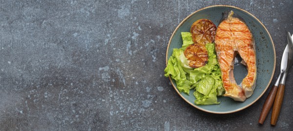 Grilled fish salmon steak and green salad with lemon on ceramic plate on rustic blue stone