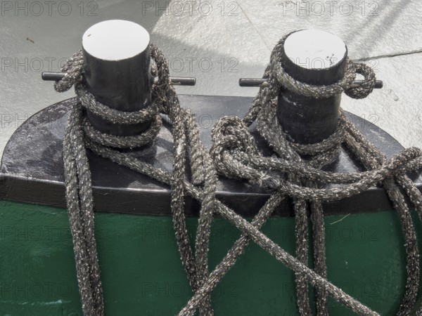 Close-up of two black metal bollards on a boat, surrounded by ropes and knots, carolinensiel,