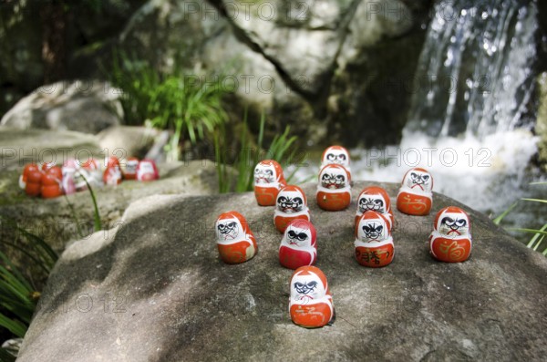 Traditional japanese Daruma dolls in front of a water fall at Katsuo Ji Temple in Mino, Japan,