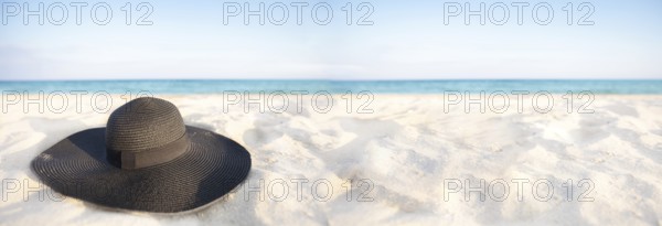 Banner Black hat on a background of the sea. Beach accessory on white sand. Straw panama on the