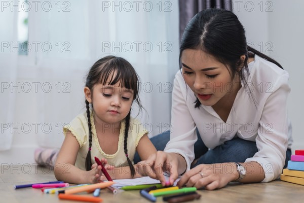 Mother teaching girl in drawing class. Daughter painting with colorful crayon color in home.