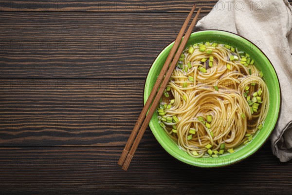 Asian noodles soup in green rustic ceramic bowl with wooden chopsticks top view on dark wooden