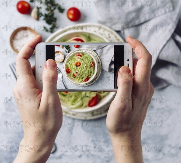 Woman hands takes top view photography of zucchini noodles salad on table with phone. Smartphone