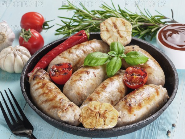Chicken homemade sausages, sauces ketchup and vegetables and herbs on blue wooden background.