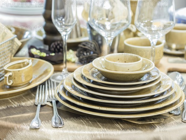 Set of new dishes on table with tablecloth. Stack of beige plates and wine glasses on restaurant