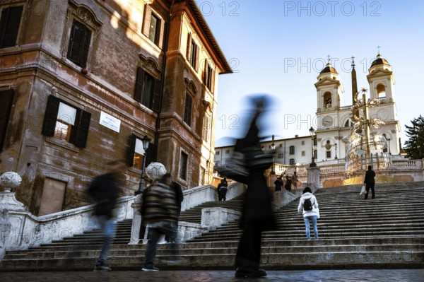People in motion on the steps of the Spanish Steps in front of historic buildings under a blue sky,