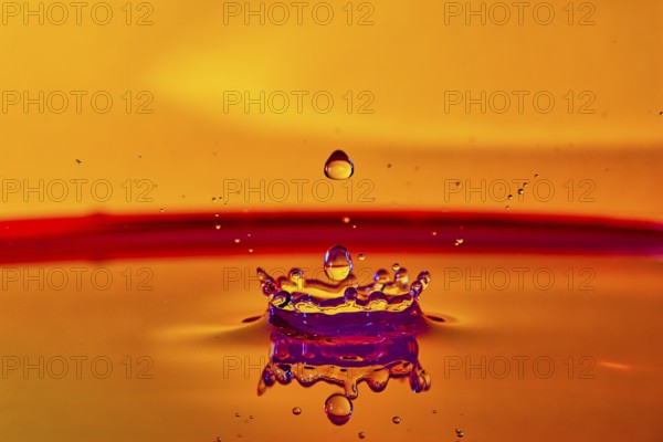 A falling drop of water creates an impressive crown on an orange-coloured surface, high-speed